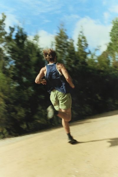 Runner on a tree-lined dirt path, motion-blurred greens, mid-stride.